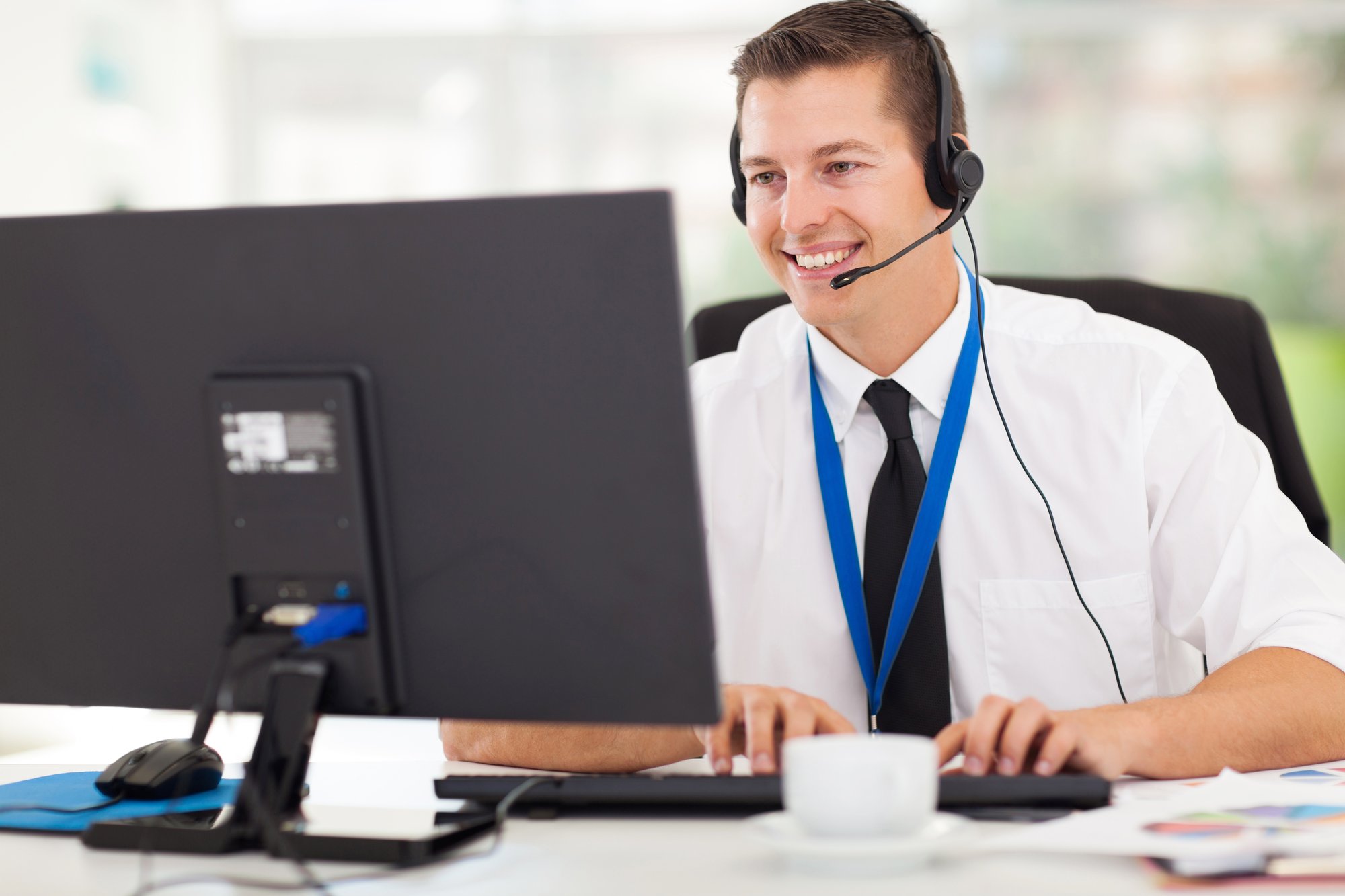 Smiling businessman wearing a headset and microphone smiles at his laptop