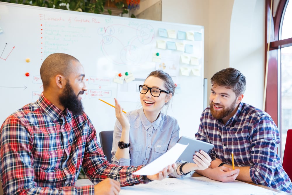 Two smiling businessmen and a smiling businesswoman in glasses brainstorm together