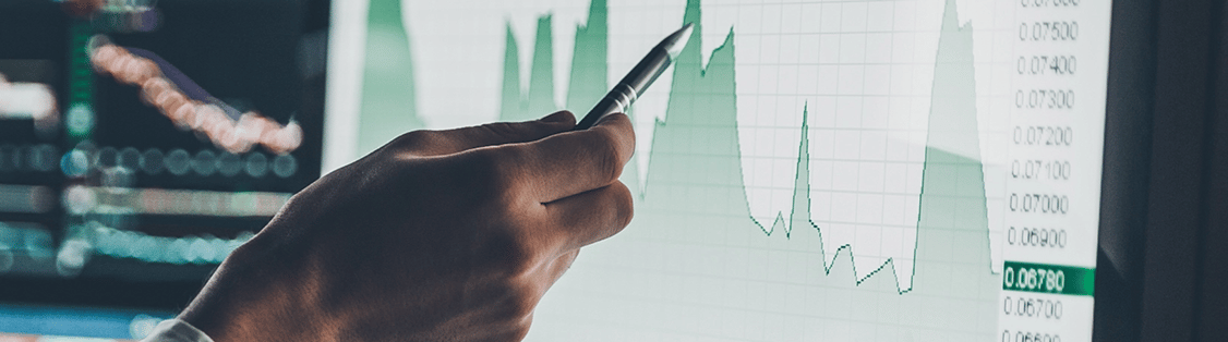 Businessman uses a pen to point at a computer screen displaying a wave graph with other charts in the background