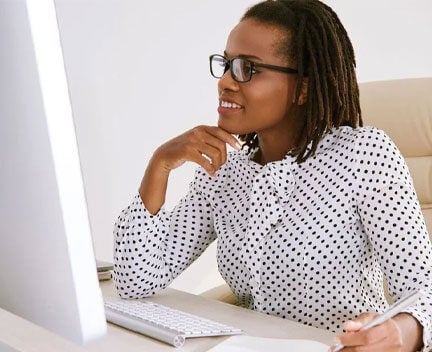 Smiling businesswoman looks at a computer screen while taking notes